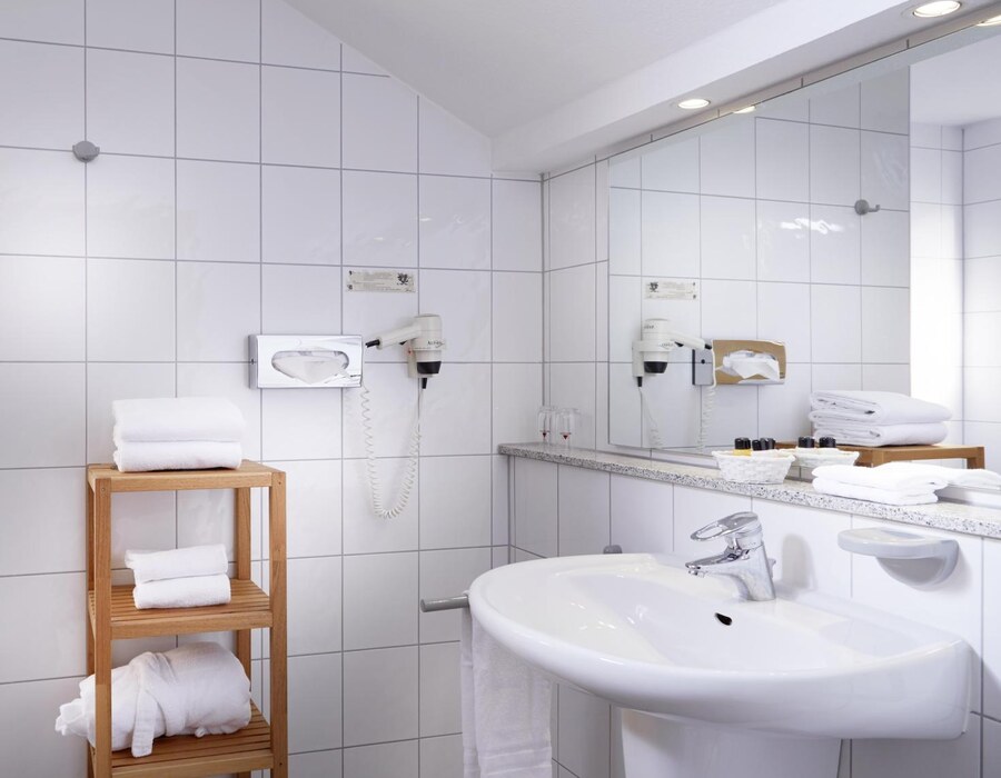 Helles Badezimmer im Gästezimmer mit Waschbecken, Spiegel, Dusche und Handtüchern