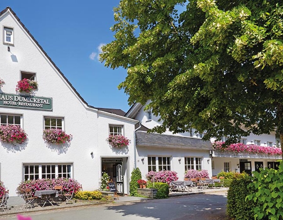 Außenansicht des Haus Dumicketal mit Biergarten, Blumen und großem Baum vor dem Gebäude
