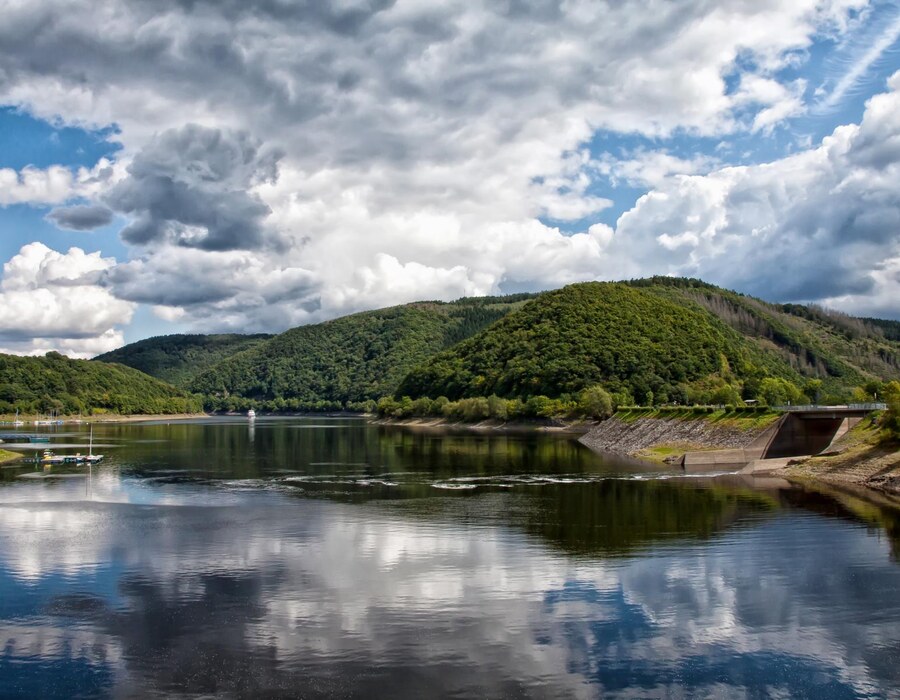 Ruhiger See im Sauerland mit bewaldeten Hügeln, Spiegelung im Wasser und bewölktem Himmel