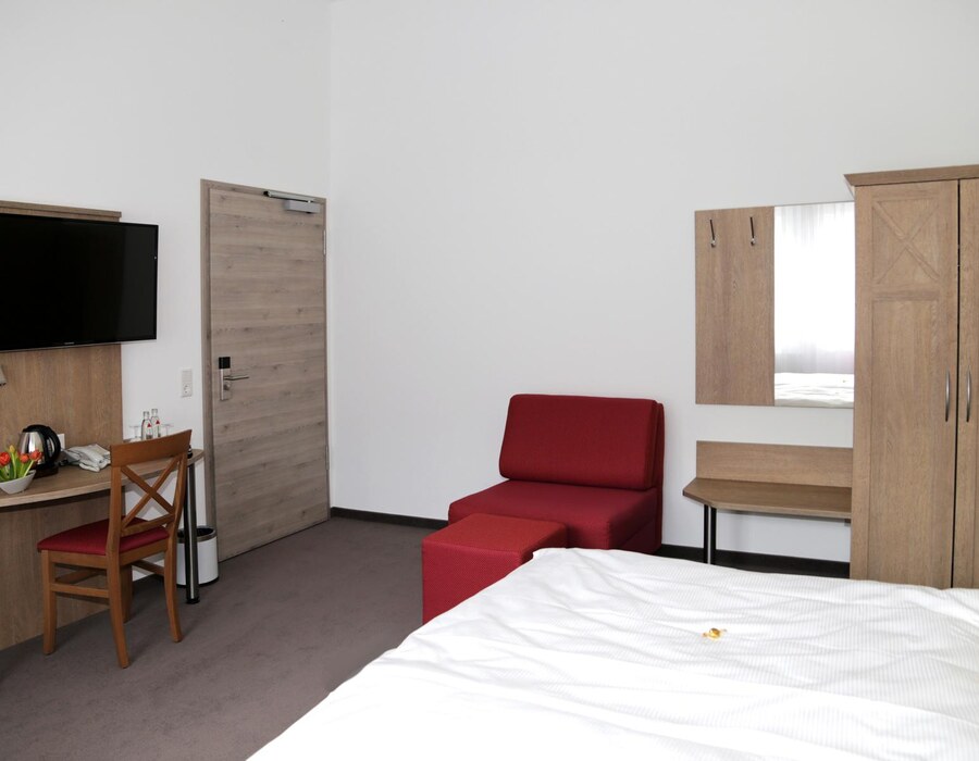 Gästezimmer im Haus Dumicketal mit Bett, Schreibtisch, Fernseher und rotem Sessel