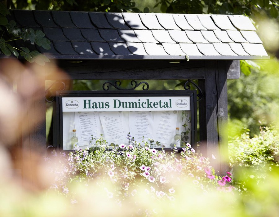 Relax Kurzurlaub Sauerland Haus Dumicketal Schild des Haus Dumicketal vor dem Hotelgarten mit Blumen im Vordergrund