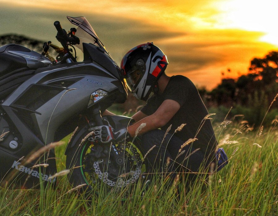 Motorradfahrer neben seinem Motorrad bei Sonnenuntergang in der Natur